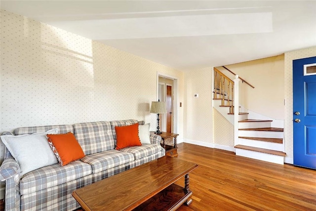 living room featuring baseboards, wallpapered walls, wood finished floors, and stairs