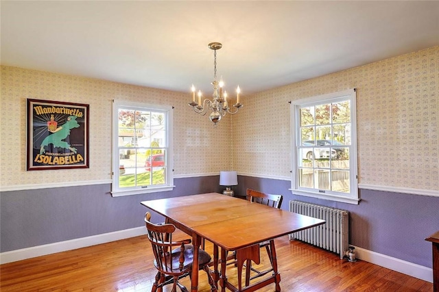 dining room featuring an inviting chandelier, wood finished floors, radiator heating unit, wallpapered walls, and a wainscoted wall