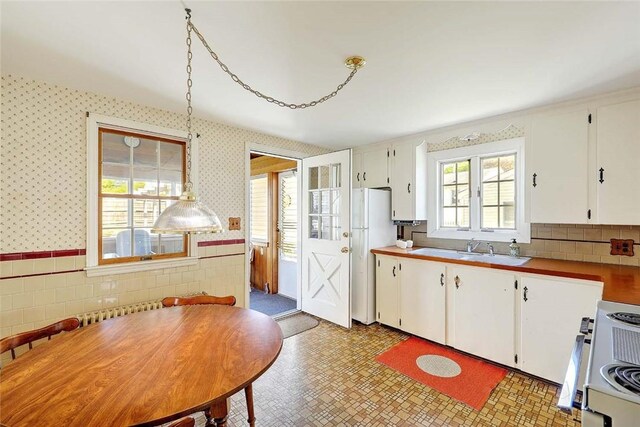kitchen with wainscoting, a sink, white appliances, white cabinetry, and wallpapered walls