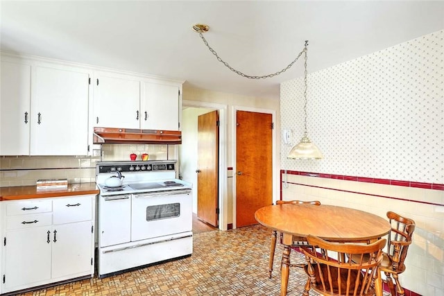kitchen featuring white cabinets, range with two ovens, wallpapered walls, and under cabinet range hood