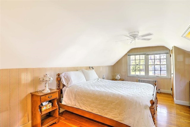 bedroom with radiator, lofted ceiling, baseboards, a ceiling fan, and light wood finished floors