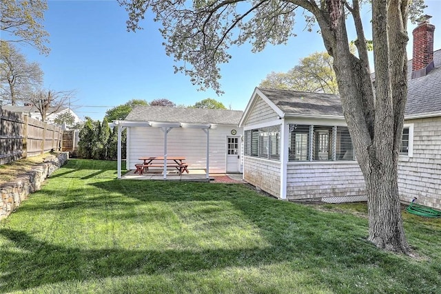 back of house featuring fence, a patio, roof with shingles, a sunroom, and a lawn