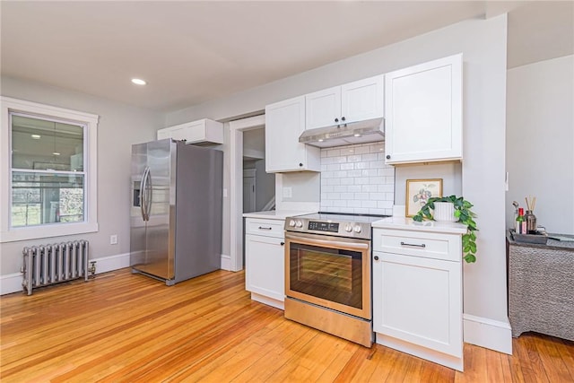 888 Providence St, West Warwick, RI 02893 - kitchen featuring appliances with stainless steel finishes, under cabinet range hood, white cabinetry, and radiator