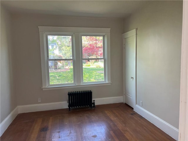 empty room featuring dark wood-style flooring, baseboards, a healthy amount of sunlight, and radiator heating unit