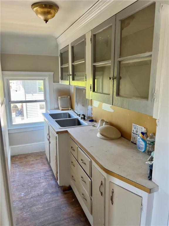 kitchen with light countertops, baseboards, a sink, glass insert cabinets, and dark wood-type flooring