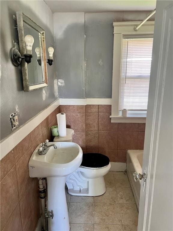 bathroom featuring tile walls, tile patterned flooring, toilet, and a tub to relax in