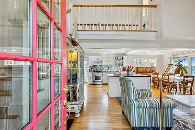 kitchen featuring a towering ceiling, white microwave, a center island, high end stove, and light wood finished floors