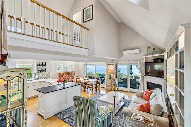 living room with a fireplace, high vaulted ceiling, a wall mounted AC, and light wood-type flooring