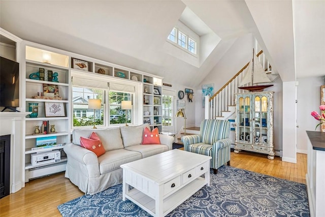living area with wood finished floors, baseboards, a high ceiling, stairway, and a baseboard heating unit