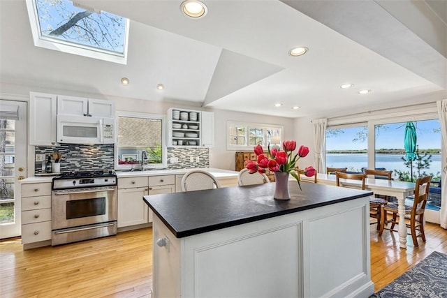 kitchen with white microwave, stainless steel gas range, tasteful backsplash, a sink, and light wood finished floors
