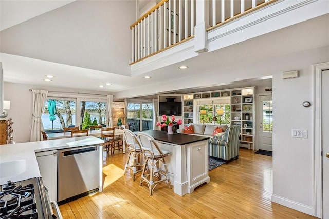 kitchen with dark countertops, stainless steel appliances, recessed lighting, light wood-type flooring, and a kitchen bar