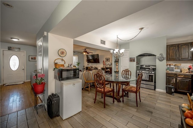 dining room with visible vents, light wood-style floors, ceiling fan with notable chandelier, and baseboards