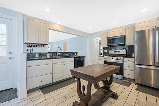 kitchen featuring dark stone counters, a sink, light wood-style flooring, backsplash, and stainless steel appliances