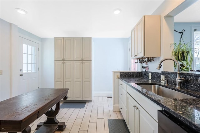 kitchen featuring a sink, dishwasher, dark stone countertops, and a healthy amount of sunlight