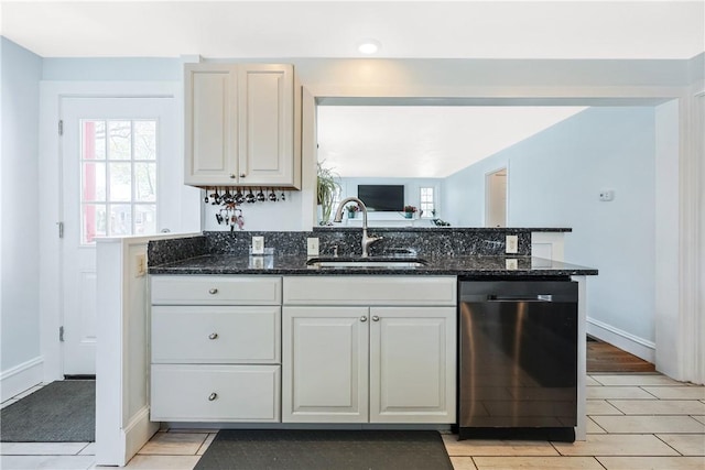 kitchen featuring stainless steel dishwasher, white cabinets, a sink, and dark stone countertops