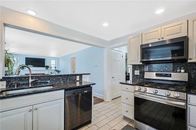 kitchen with a sink, decorative backsplash, dark stone counters, and stainless steel appliances