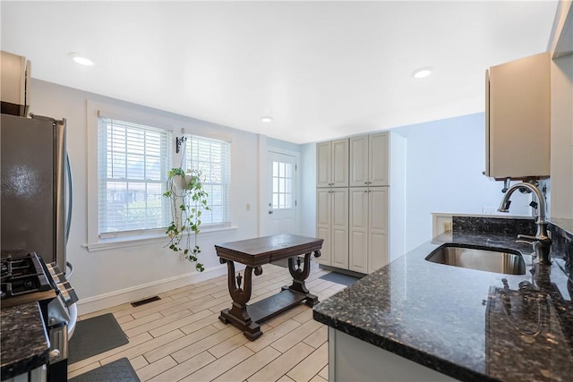 kitchen with a sink, dark stone countertops, freestanding refrigerator, baseboards, and visible vents