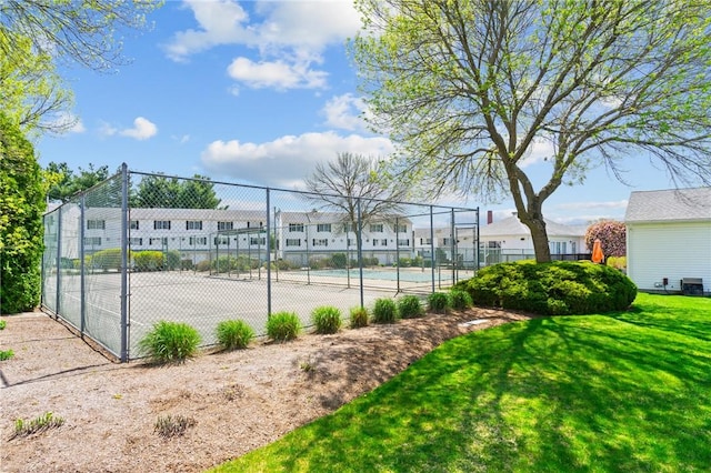 view of tennis court with fence, a yard, and a residential view