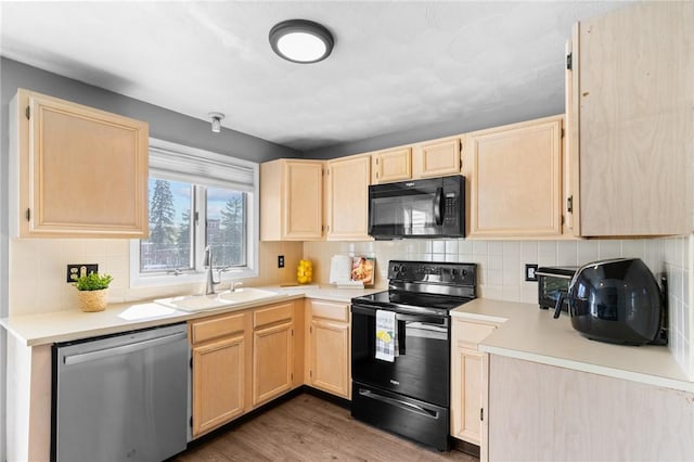 kitchen with wood finished floors, a sink, light brown cabinetry, and black appliances