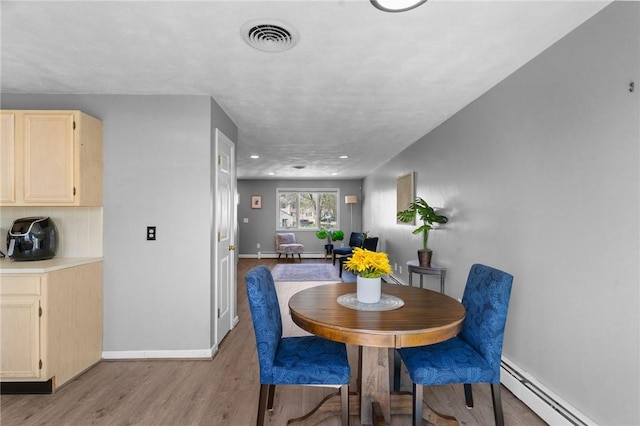 dining room with baseboards, a baseboard heating unit, light wood finished floors, and visible vents