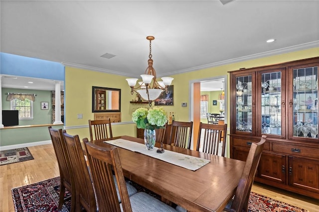dining area featuring an inviting chandelier, light wood-style flooring, baseboards, ornate columns, and ornamental molding