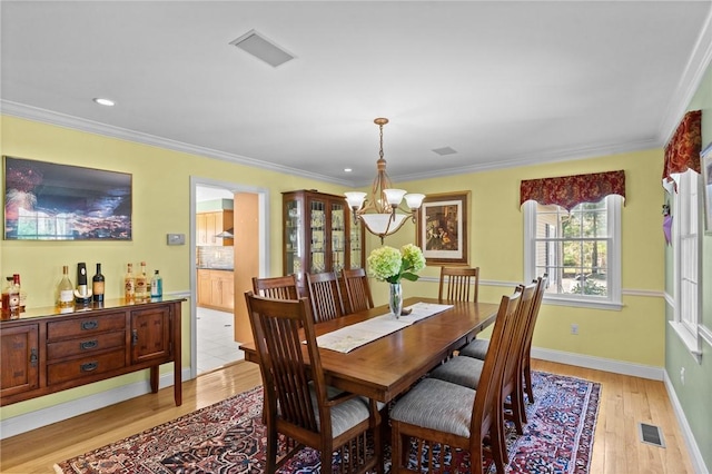 dining area with visible vents, ornamental molding, a notable chandelier, and light wood-type flooring
