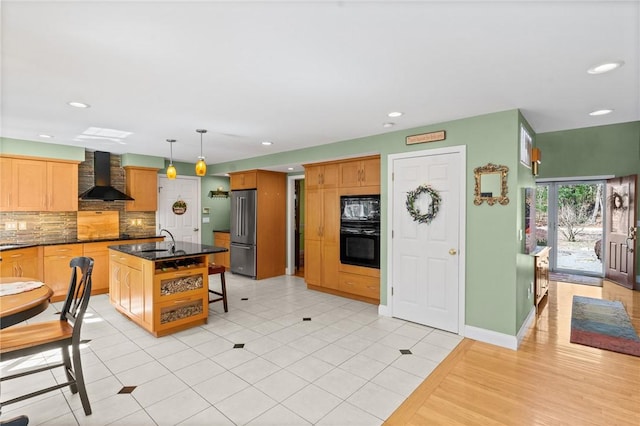 kitchen with a sink, high end refrigerator, wall chimney exhaust hood, recessed lighting, and backsplash