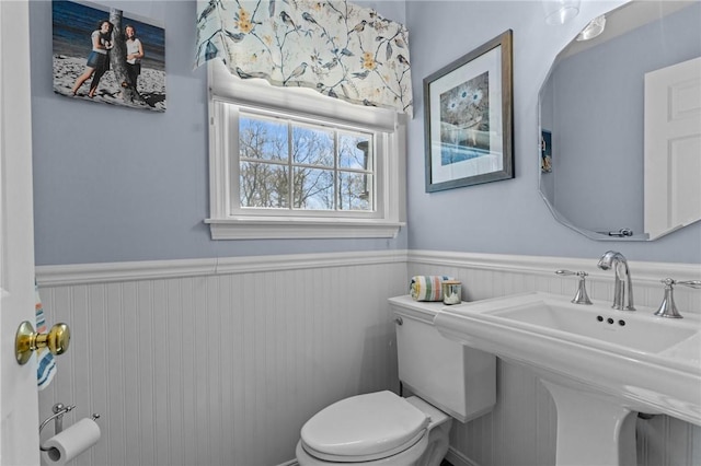 bathroom featuring toilet, a sink, and a wainscoted wall