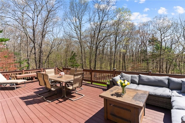 wooden terrace with an outdoor living space, a wooded view, and outdoor dining space