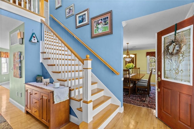 stairway featuring baseboards, an inviting chandelier, a healthy amount of sunlight, and wood finished floors
