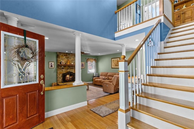 foyer featuring a stone fireplace, stairs, baseboards, decorative columns, and wood finished floors