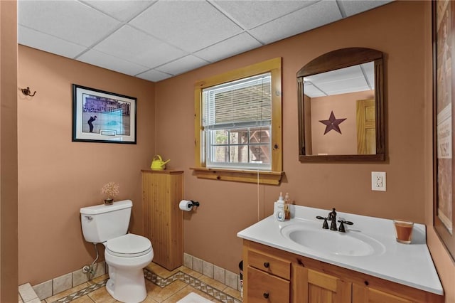 half bath featuring vanity, toilet, baseboards, a paneled ceiling, and tile patterned floors