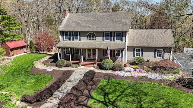 colonial inspired home with a shingled roof, a chimney, a porch, and a front yard