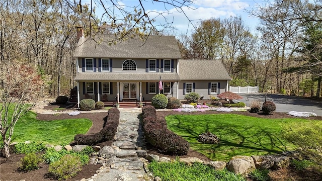 view of front of home with covered porch, a chimney, roof with shingles, fence, and a front lawn