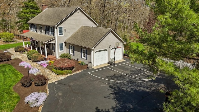 view of front of property featuring a garage, aphalt driveway, roof with shingles, a chimney, and a porch