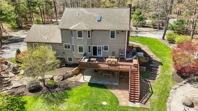 rear view of house featuring a patio area, a wooden deck, a yard, and roof with shingles