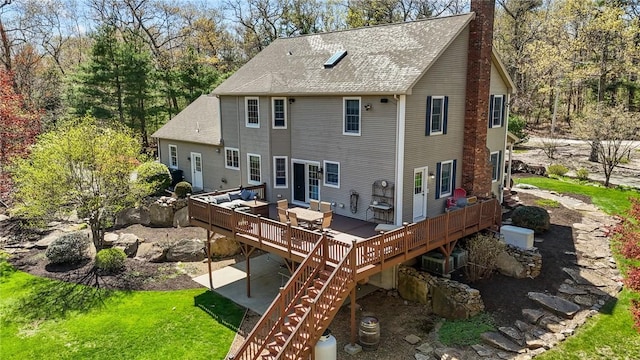 rear view of property featuring a chimney, roof with shingles, a wooden deck, a patio area, and stairs
