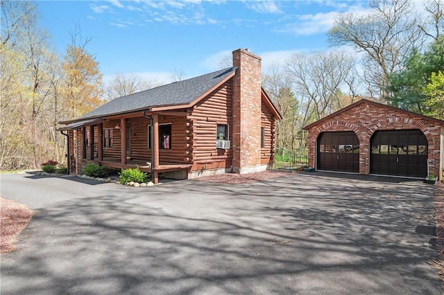 view of side of home featuring roof with shingles, log siding, an outbuilding, a chimney, and covered porch