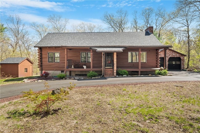 log-style house with an outdoor structure, log exterior, a chimney, covered porch, and driveway