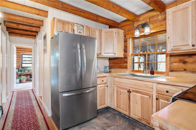 kitchen with freestanding refrigerator, rustic walls, beam ceiling, light brown cabinets, and a sink