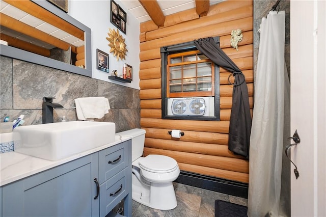 bathroom featuring a shower with curtain, beam ceiling, vanity, toilet, and rustic walls