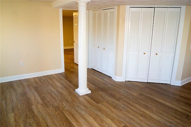 unfurnished bedroom featuring baseboards, two closets, dark wood-style flooring, and ornate columns