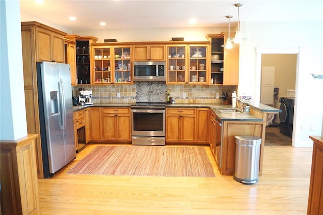 kitchen featuring brown cabinets, a sink, light wood finished floors, a peninsula, and stainless steel appliances