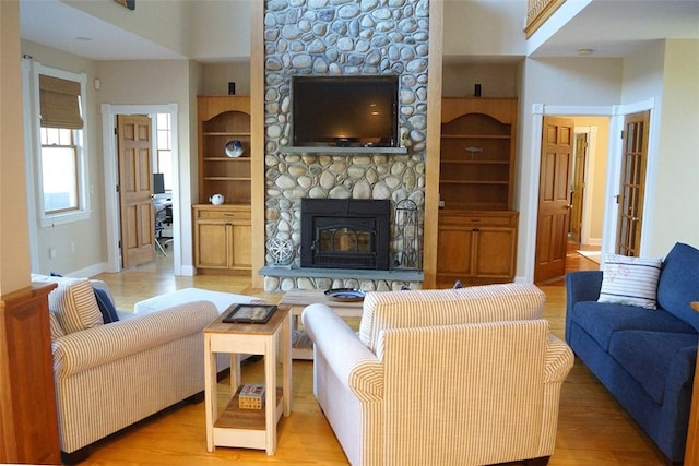 living area with baseboards, a stone fireplace, built in features, and light wood finished floors