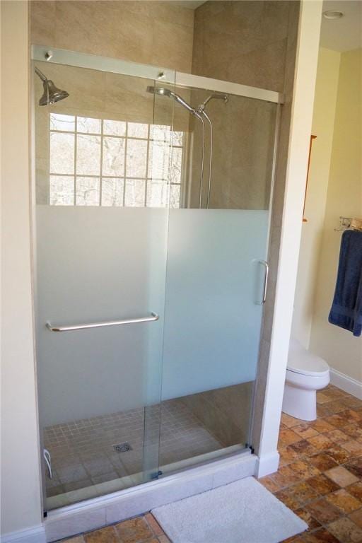 bathroom with toilet, baseboards, and a shower stall