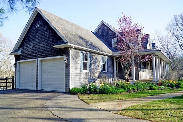 view of property exterior featuring covered porch, fence, a shingled roof, and a garage