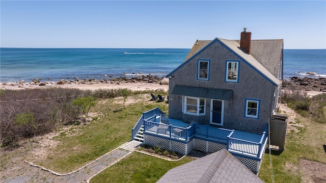 exterior space featuring a deck with water view, a view of the beach, a chimney, and a shingled roof