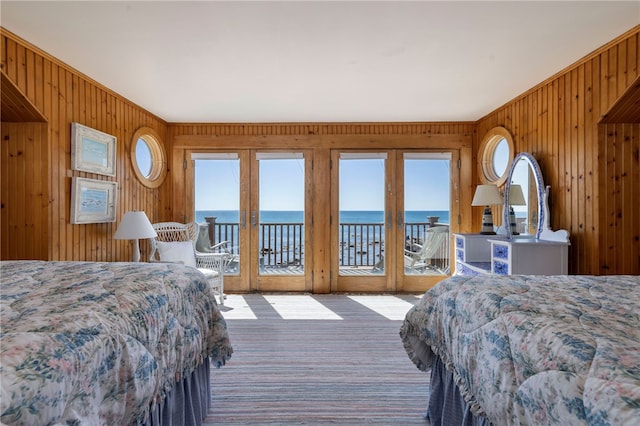 carpeted bedroom with a water view, french doors, and wood walls