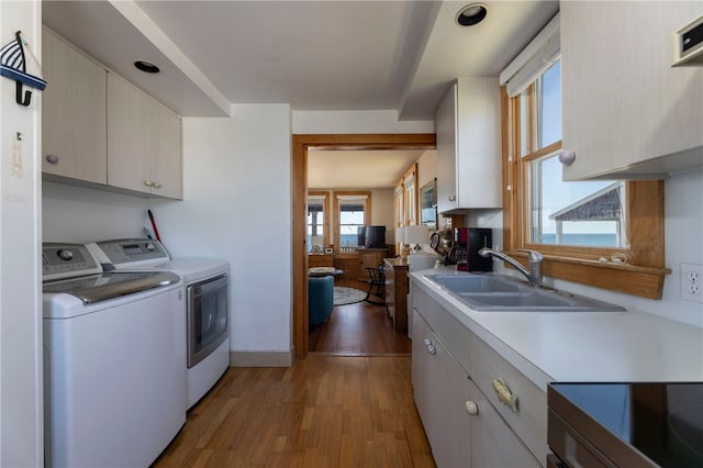 kitchen with independent washer and dryer, a sink, light wood finished floors, light countertops, and a healthy amount of sunlight
