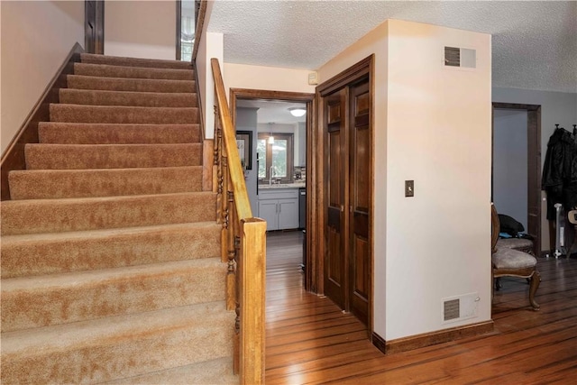 stairs with visible vents, baseboards, a textured ceiling, and wood finished floors